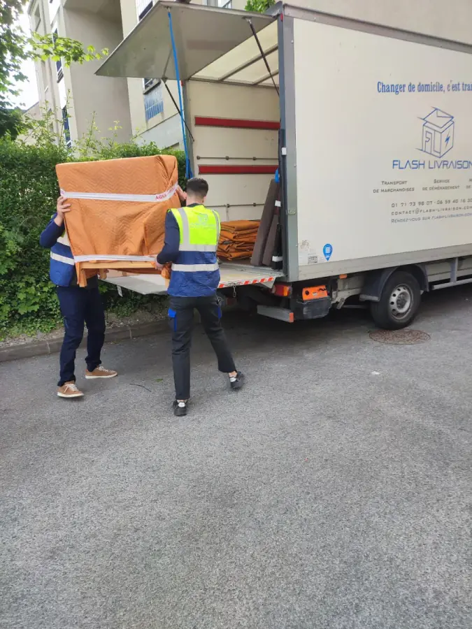 Deux déménageurs portant un meuble protégé vers le véhicule Deux déménageurs portant un meuble protégé vers le véhicule